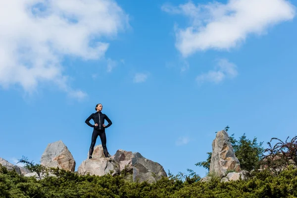 Donna in piedi su rocce con le braccia akimbo — Foto stock