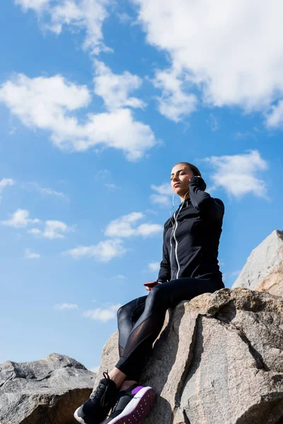 Woman sitting on rocks and listening music — Stock Photo