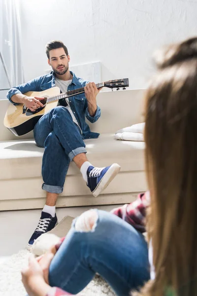 Молодой человек на диване играет на гитаре — стоковое фото