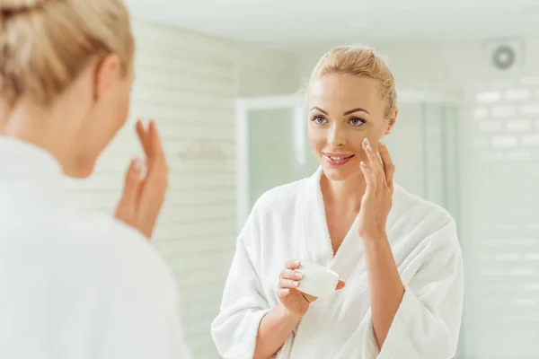 Mujer en albornoz aplicando crema facial - foto de stock