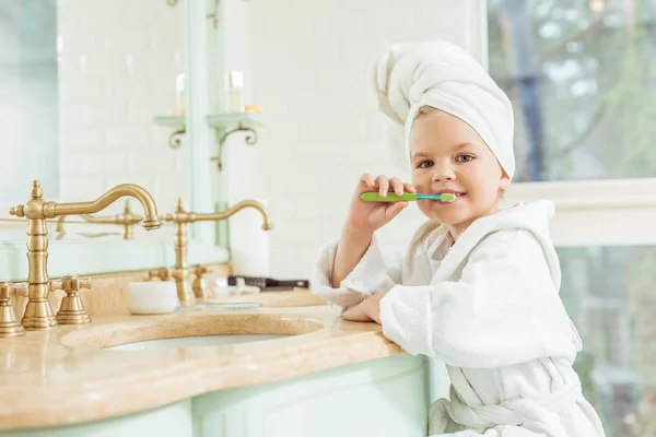 Niño en albornoz cepillarse los dientes - foto de stock