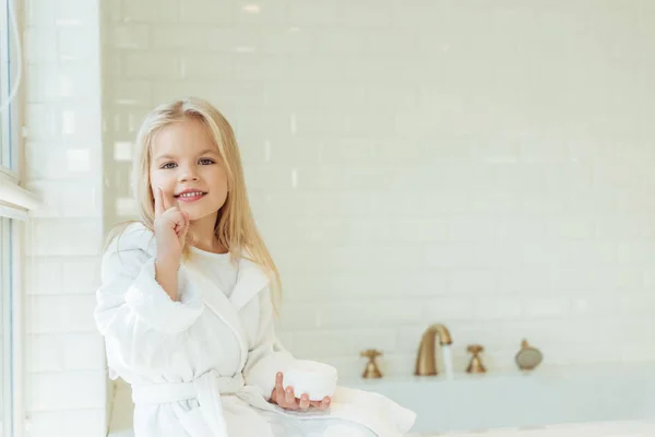 Enfant en peignoir appliquant crème visage — Photo de stock