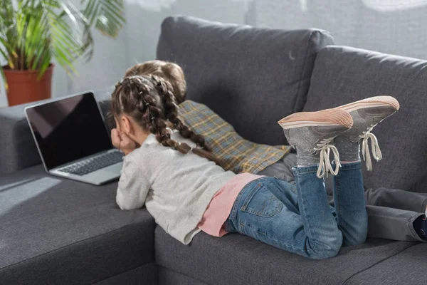 Kids lying on sofa with laptop — Stock Photo