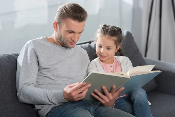 Батько навчає доньку читати вдома — стокове фото
