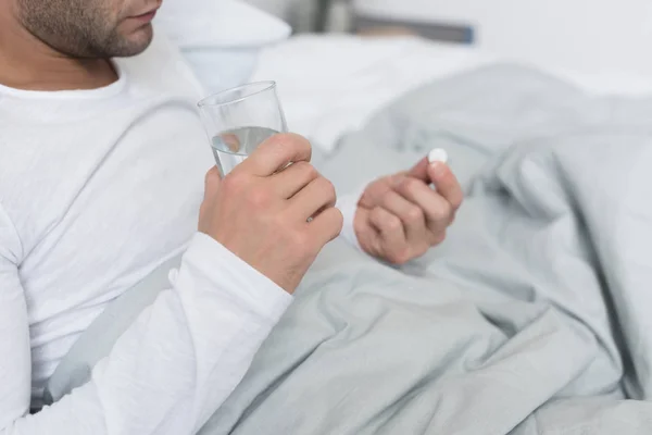 Больной человек держит таблетки и стекло — стоковое фото