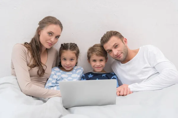 Родина лежить в ліжку з ноутбуком — стокове фото