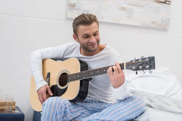 Uomo che suona la chitarra sul letto — Foto stock