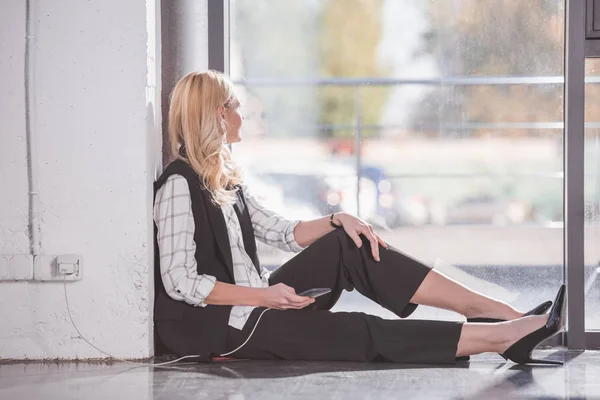 Femme d'affaires assis sur le sol et téléphone de charge — Photo de stock