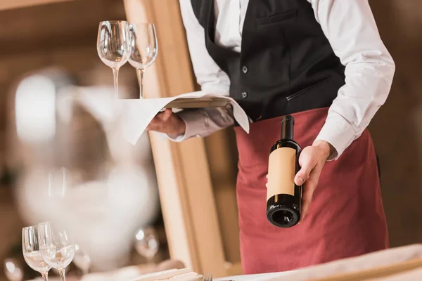 Garçom segurando vinhos e garrafa — Fotografia de Stock