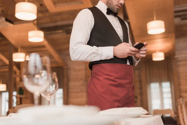 Официант стоит и смотрит на смартфон — стоковое фото