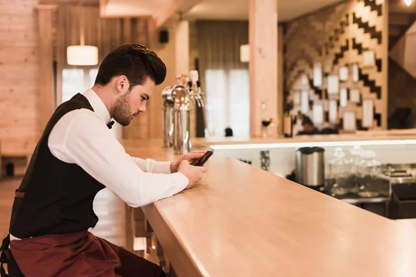 Waiter sitting at bar counter with smartphone — Stock Photo