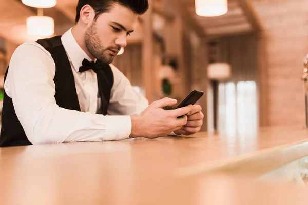 Официант сидит за барной стойкой со смартфоном — стоковое фото