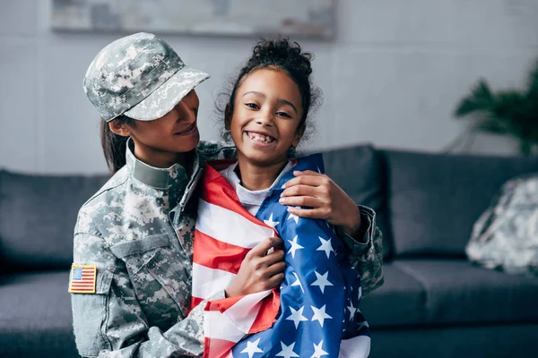 Soldier and daughter wrapped with american flag — Stock Photo