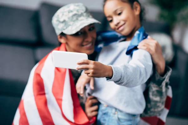 Hija y soldado con bandera tomando selfie - foto de stock