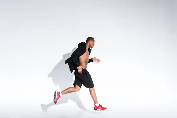 Вид збоку молодого афроамериканця в спортивному одязі, що біжить на сірому — стокове фото