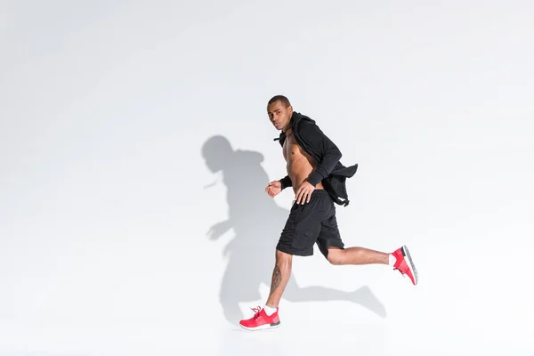 Joven afroamericano deportista corriendo y mirando a la cámara en gris — Stock Photo