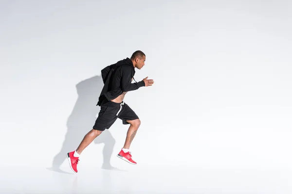 Vista lateral de joven afroamericano deportista en ropa deportiva corriendo en gris - foto de stock
