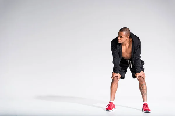 Vue pleine longueur du jeune sportif afro-américain en sweat à capuche et baskets regardant loin sur gris — Photo de stock