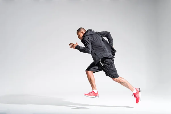 Vue latérale du jeune sportif afro-américain qui court sur le gris — Photo de stock