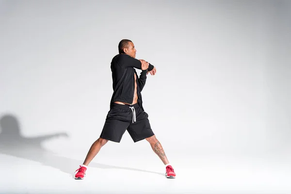 Vista completa de joven atlético afroamericano deportista estiramiento en gris - foto de stock