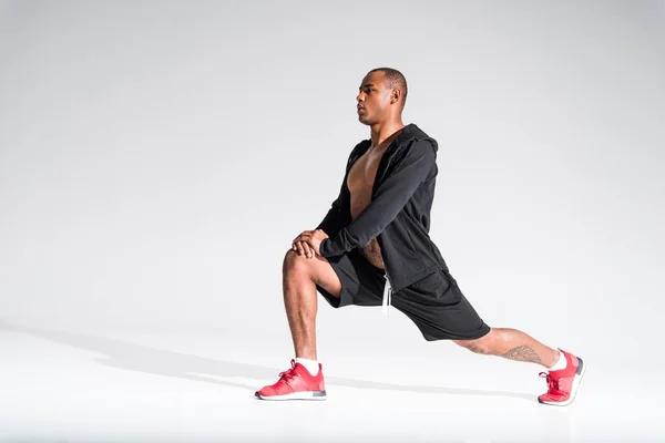 Athletic young african american sportsman stretching and looking away on grey — Stock Photo