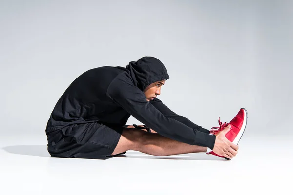 Side view of young african american sportsman stretching on grey — Stock Photo