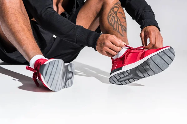 Cropped shot of african american sportsman tying shoelaces on grey — Stock Photo