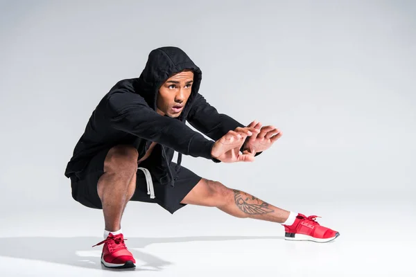 Ganzkörperansicht des jungen afrikanisch-amerikanischen Sportlers, der sich streckt und auf grau wegschaut — Stockfoto