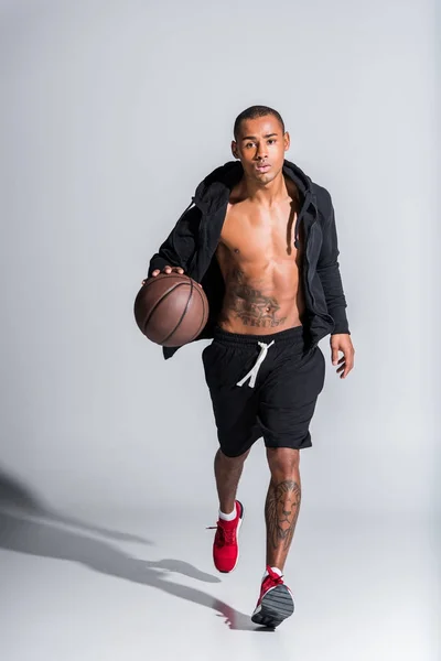 Giovane sportivo afroamericano con pallone da basket guardando la macchina fotografica sul grigio — Foto stock