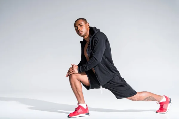 Handsome young african american sportsman stretching and looking at camera on grey — Stock Photo