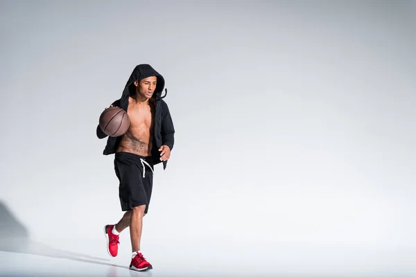 Sportif jeune homme afro-américain en vêtements de sport jouer avec ballon de basket-ball sur gris — Photo de stock