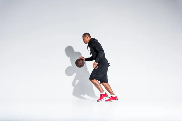 Visão de comprimento total do jovem esportista afro-americano jogando com bola de basquete em cinza — Fotografia de Stock