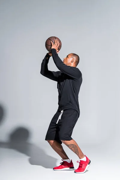 Joven deportista afroamericano jugando con pelota de baloncesto en gris - foto de stock