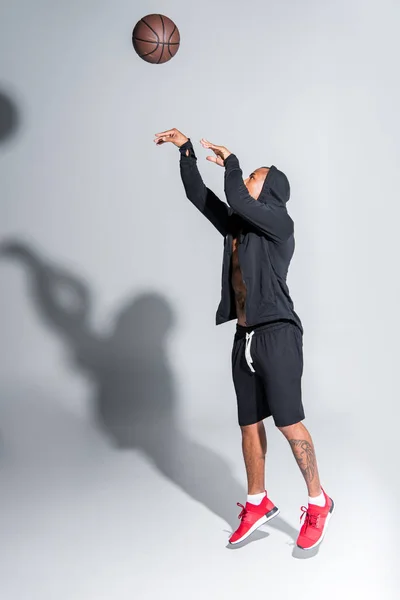 Junger afrikanisch-amerikanischer Mann in Sportbekleidung spielt mit Basketballball auf grau — Stockfoto