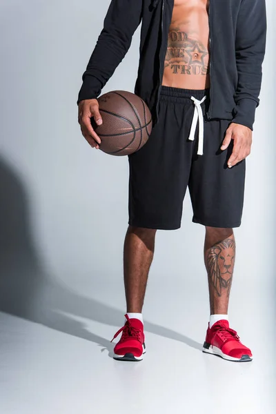 Обрізаний знімок афроамериканця, який тримає баскетбольний м'яч на сірому — стокове фото