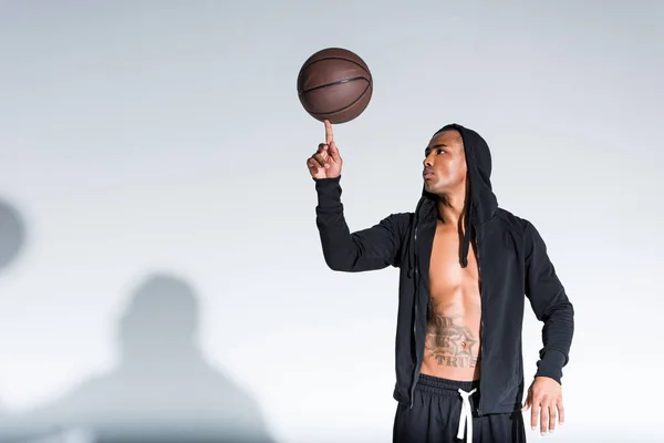 Афроамериканський чоловік тримає баскетбольну кулю на пальці на сірому — стокове фото