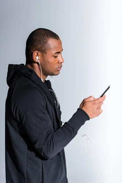 Seitenansicht eines jungen afrikanisch-amerikanischen Mannes mit Smartphone auf grau — Stockfoto
