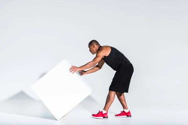 Junger afrikanisch-amerikanischer Sportler bewegt White Cube auf Grau — Stockfoto