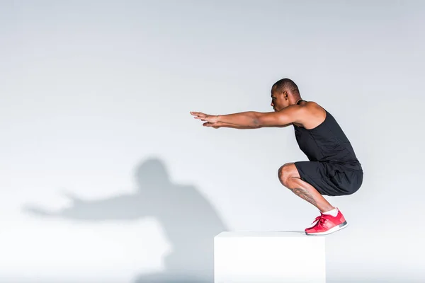 Vue latérale du jeune sportif afro-américain prêt à sauter sur le gris — Photo de stock