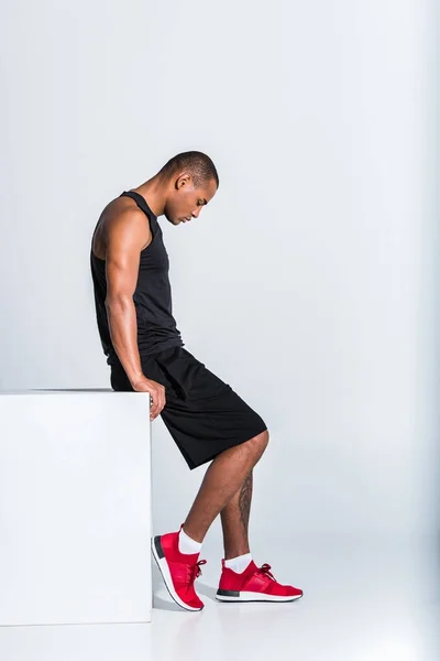 Side view of young african american sportsman sitting and looking down isolated on grey — Stock Photo