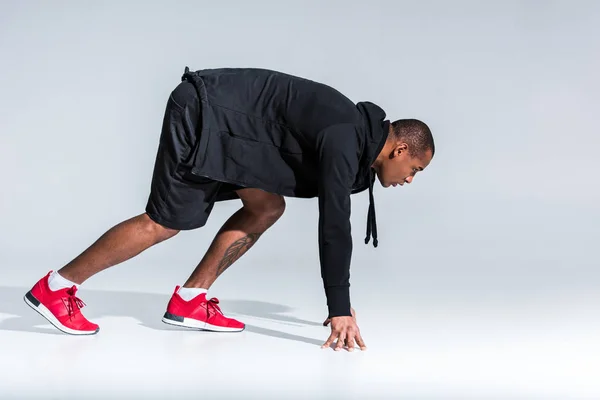 Vue latérale du jeune sportif afro-américain en sweat à capuche prêt à courir sur gris — Photo de stock