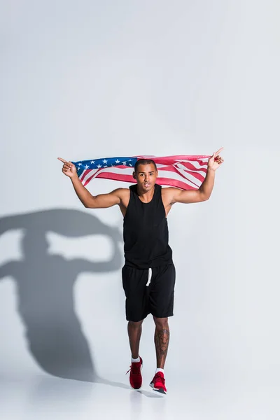 Молодой африканский американский спортсмен, держащий американский флаг и бегущий на сером — стоковое фото