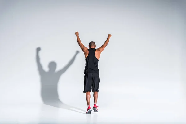 Rückseite des athletischen afrikanisch-amerikanischen Sportlers triumphiert mit erhobenen Händen auf grau — Stockfoto