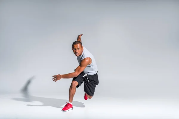 Jeune sportif afro-américain courant et regardant la caméra sur gris — Photo de stock