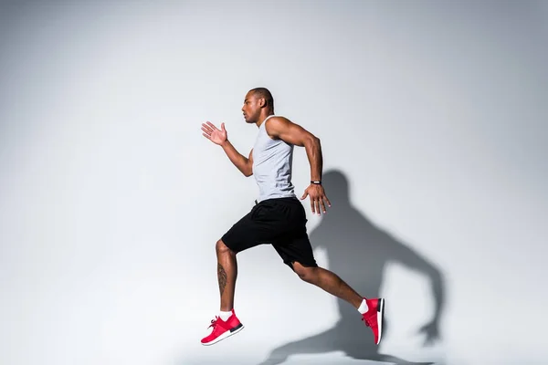 Vista lateral del joven deportista afroamericano corriendo sobre gris — Stock Photo