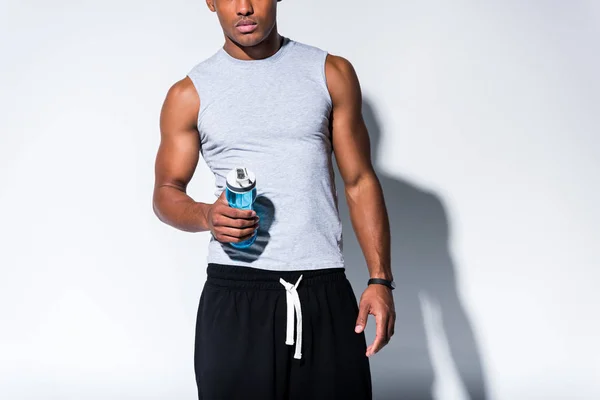 Cropped shot of young african american sportsman holding sports bottle with water on grey — Stock Photo