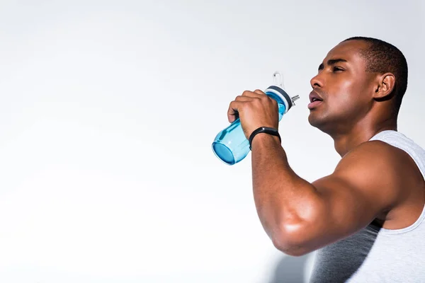 Junger afrikanisch-amerikanischer Sportler trinkt Wasser aus Sportflasche auf grau — Stockfoto