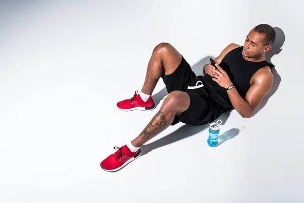 Hochwinkelaufnahme eines gutaussehenden afrikanisch-amerikanischen Sportlers mit Smartphone auf grau — Stockfoto