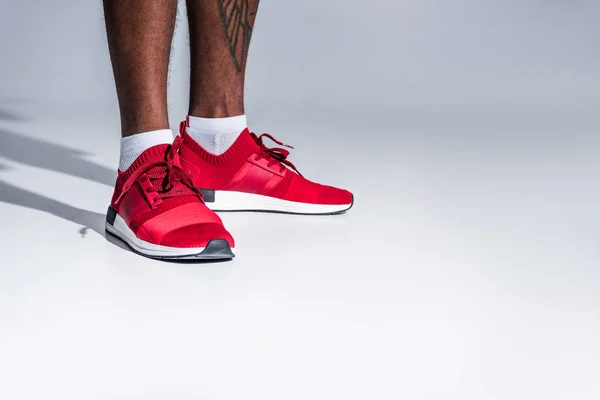 Close-up partial view of african american man in sports shoes standing isolated on grey — Stock Photo