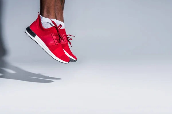 Cropped shot of young african american sportsman in sneakers jumping on grey — Stock Photo